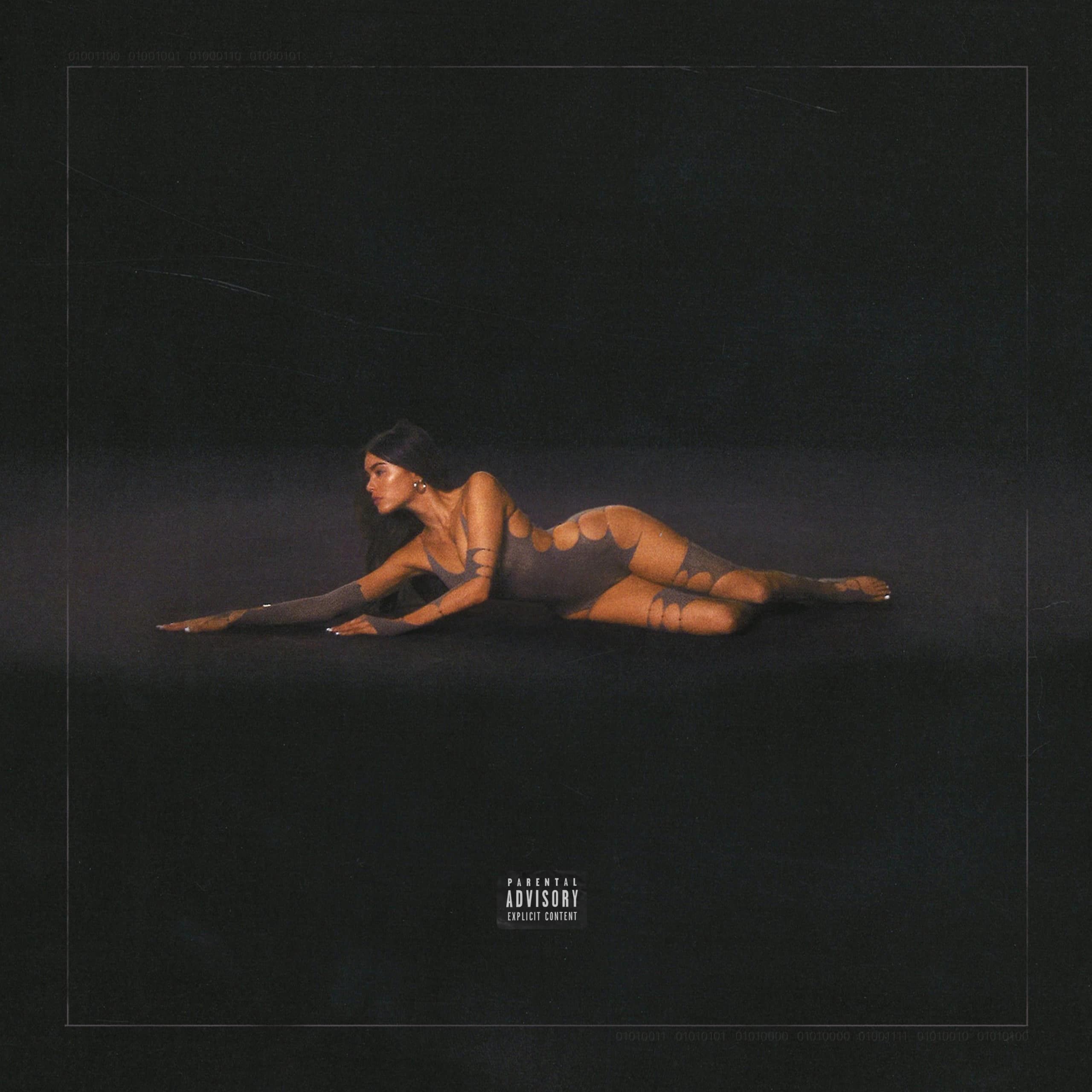 Madison Beer stretched out along a black floor in a grey bodysuit