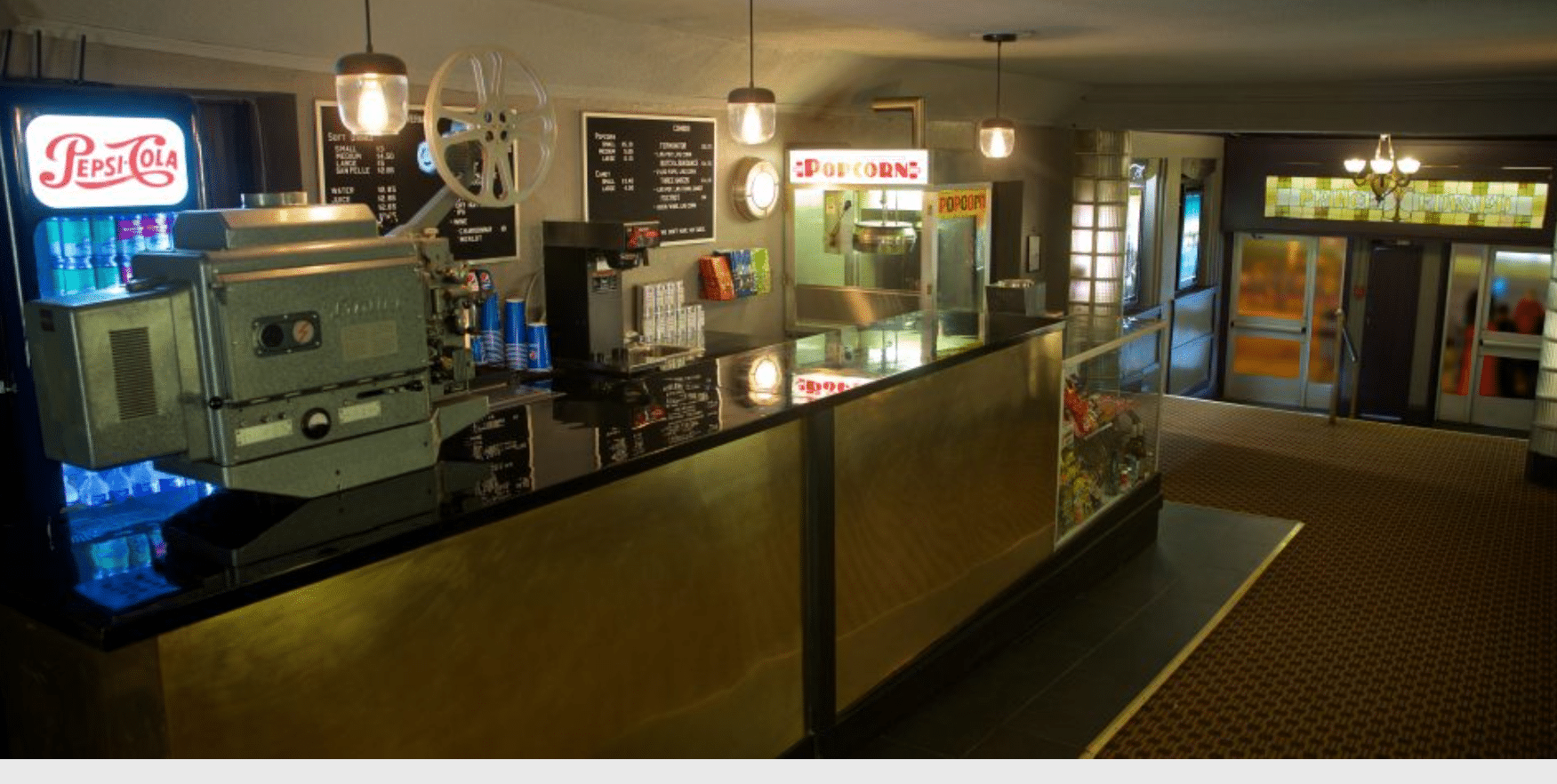 A concession table with a film projector and cash register in a half-lit room.