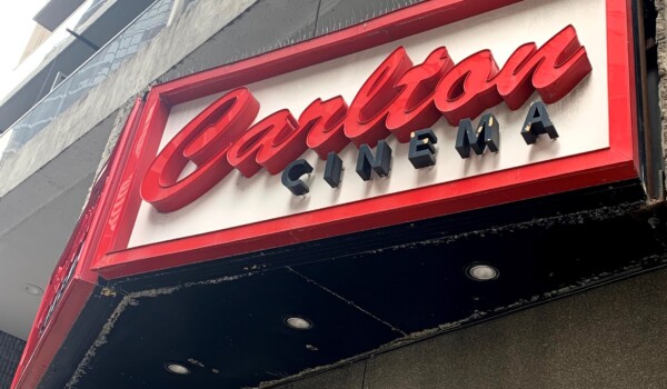 Red and black letters on a white sign on an elevated wall outside.