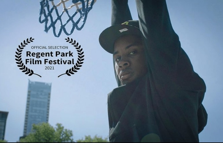 A man is hanging on a basketball net outdoors.
