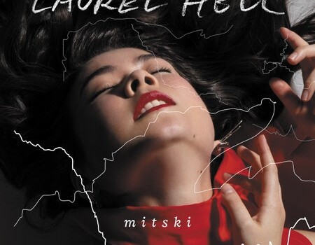 Mitski in a red turtleneck, holding up her hands with her hair spread out